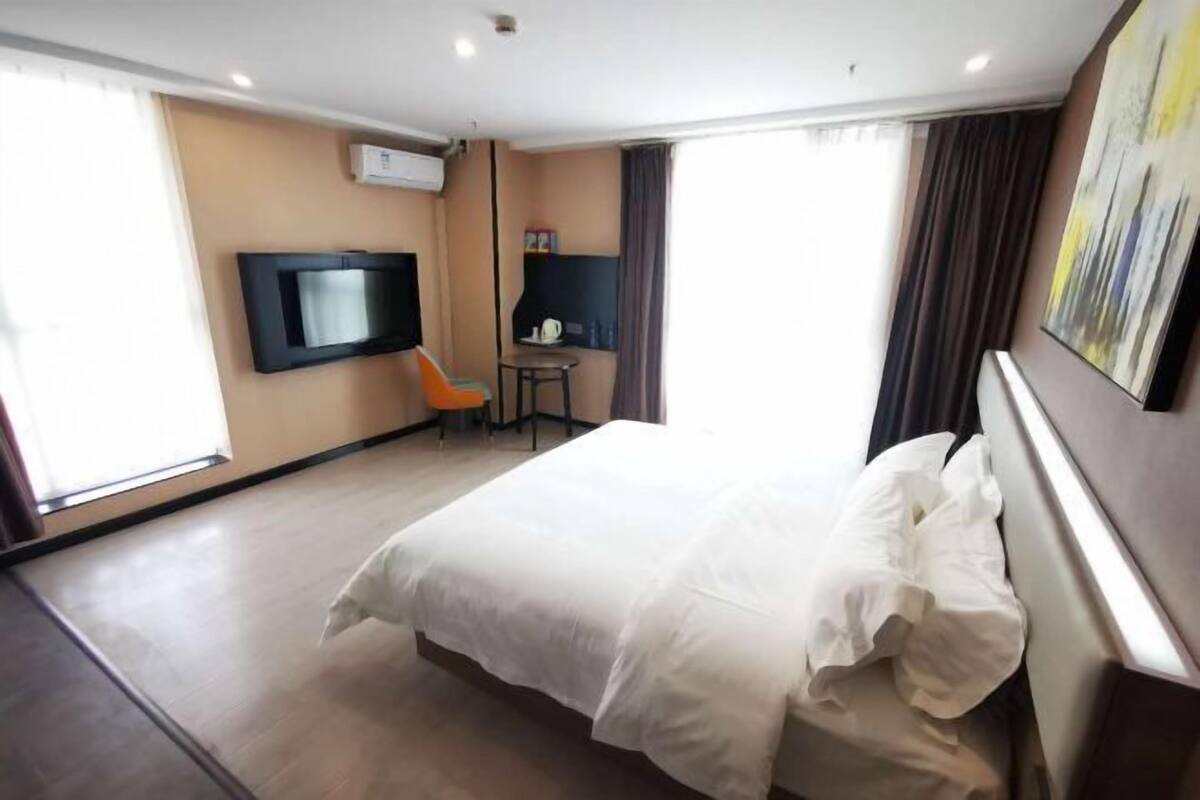 Une chambre d’hôtel avec un lit, un téléviseur fixé au mur, une petite table avec une chaise et une fenêtre avec des rideaux.
