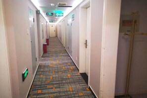 Un pasillo de hotel con puertas a ambos lados, piso alfombrado y señal de salida de emergencia.