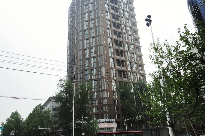 A tall, multi-story building with a grid-like facade, surrounded by trees and street infrastructure.