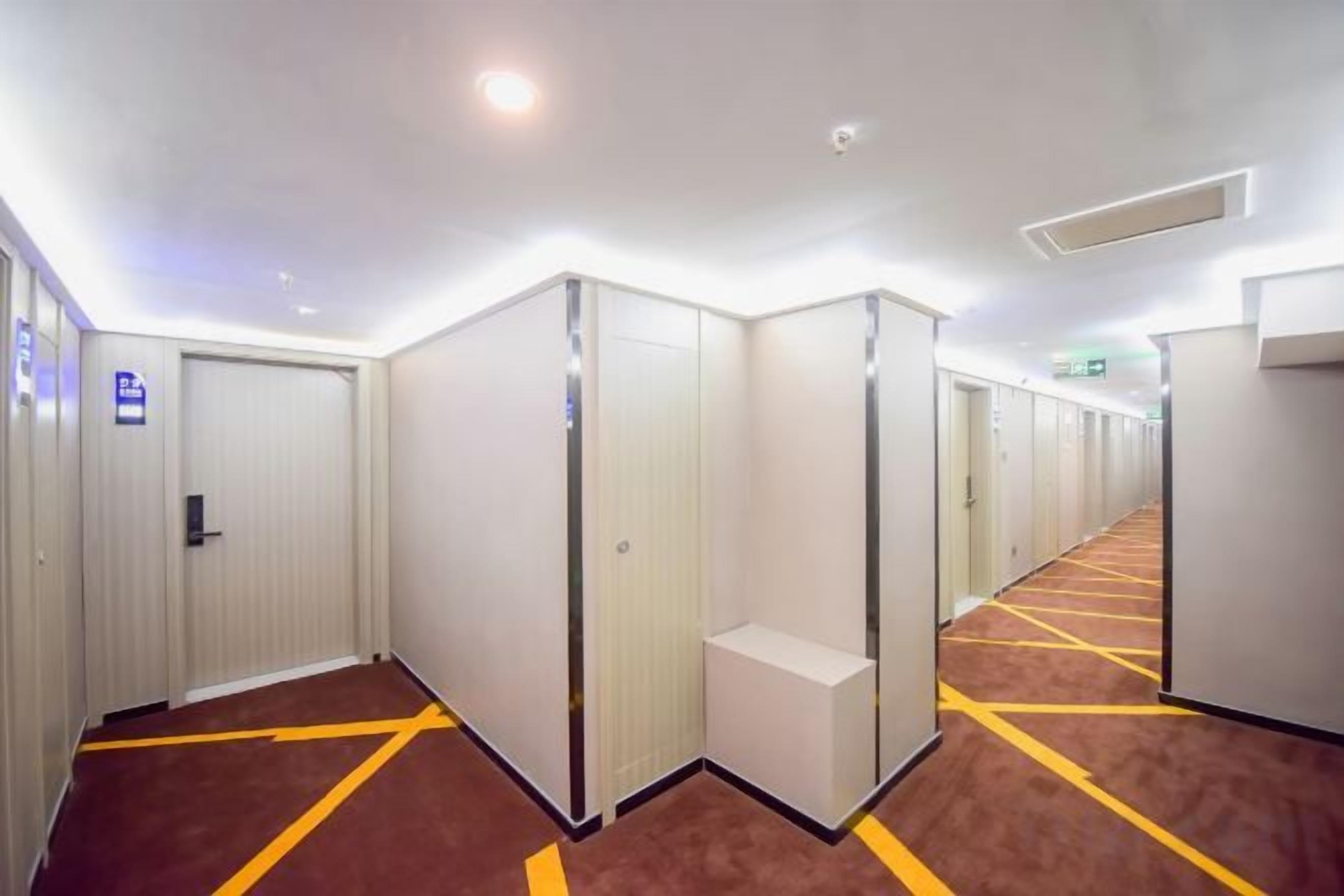 Un couloir d’hôtel avec de nombreuses chambres, un sol recouvert de moquette et une porte avec une pancarte.