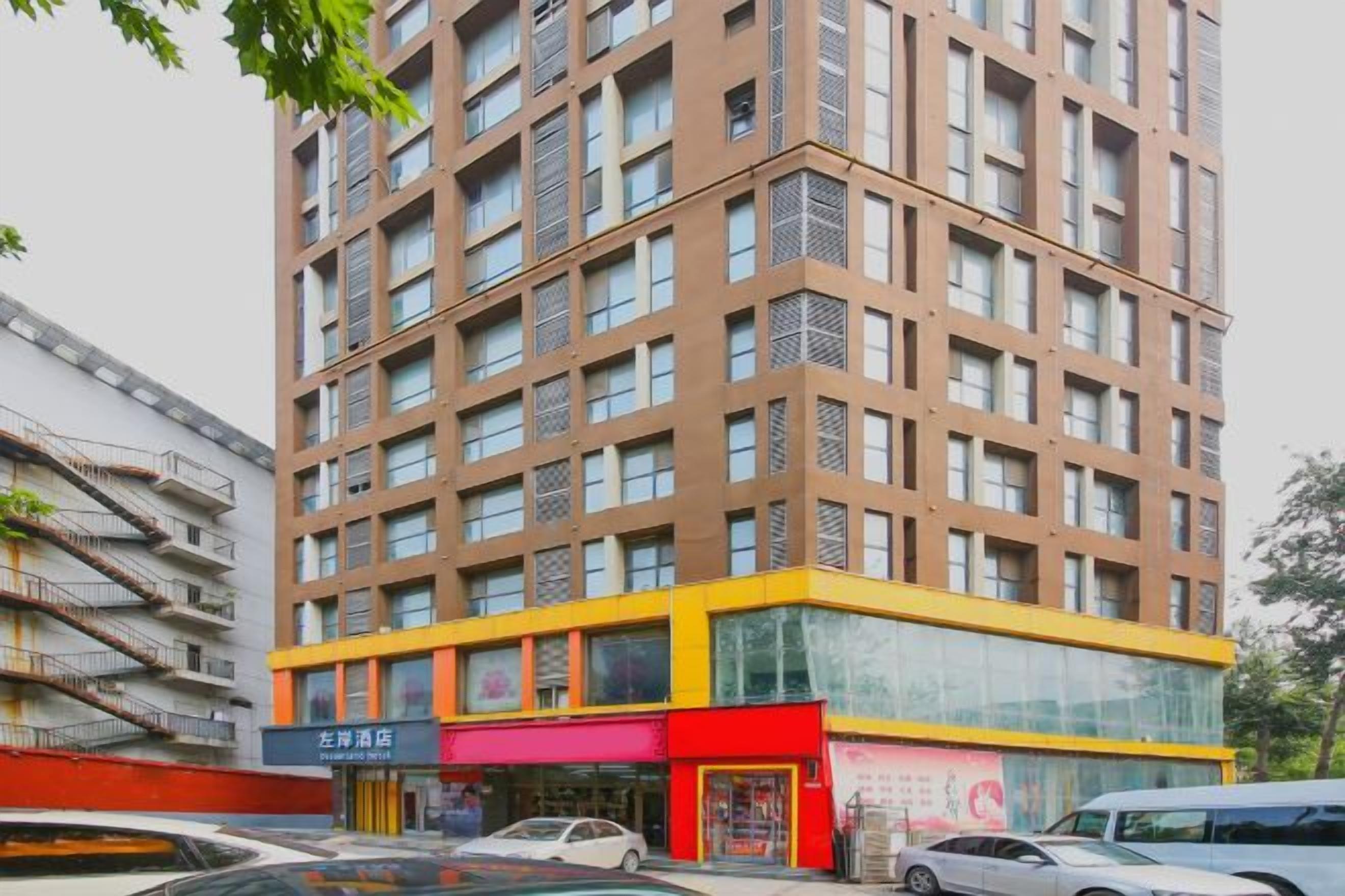 Ein mehrstöckiges Gebäude mit moderner Architektur, das eine auffällige Fassade in Gelb und Rot sowie einen im Erdgeschoss gelegenen Geschäftsraum mit Beschilderung zeigt.