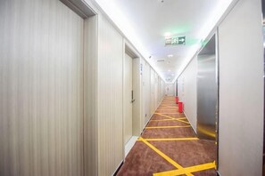 Un couloir d’hôtel avec des portes des deux côtés, un sol recouvert de moquette et un ascenseur sur la droite.