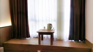 Una habitación con una mesa de madera, una tetera blanca y una ventana con cortinas translúcidas.