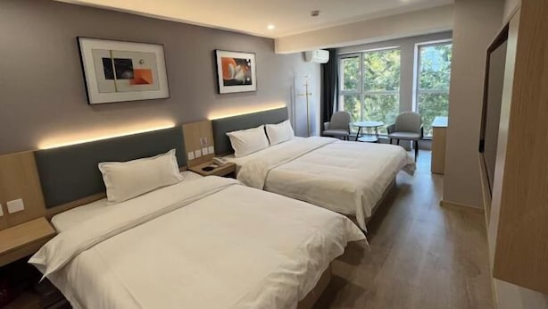 Habitación de hotel con dos camas, un escritorio, una silla y ventana con vista a árboles.