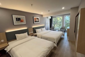 Une chambre d’hôtel avec deux lits, un bureau, une chaise et une fenêtre donnant sur des arbres.