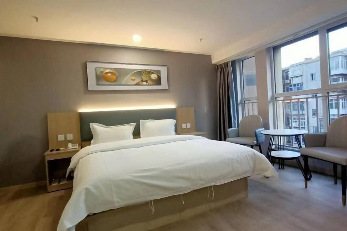 Une chambre d’hôtel avec un grand lit, des tables de chevet, une chaise, une petite table et une fenêtre avec des rideaux.