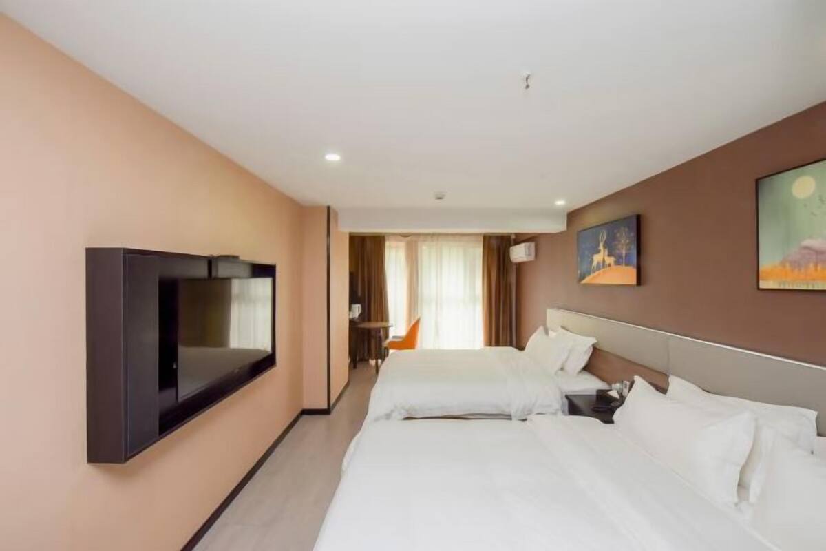 Une chambre d’hôtel avec deux lits, un téléviseur fixé au mur et un tableau accroché au mur.