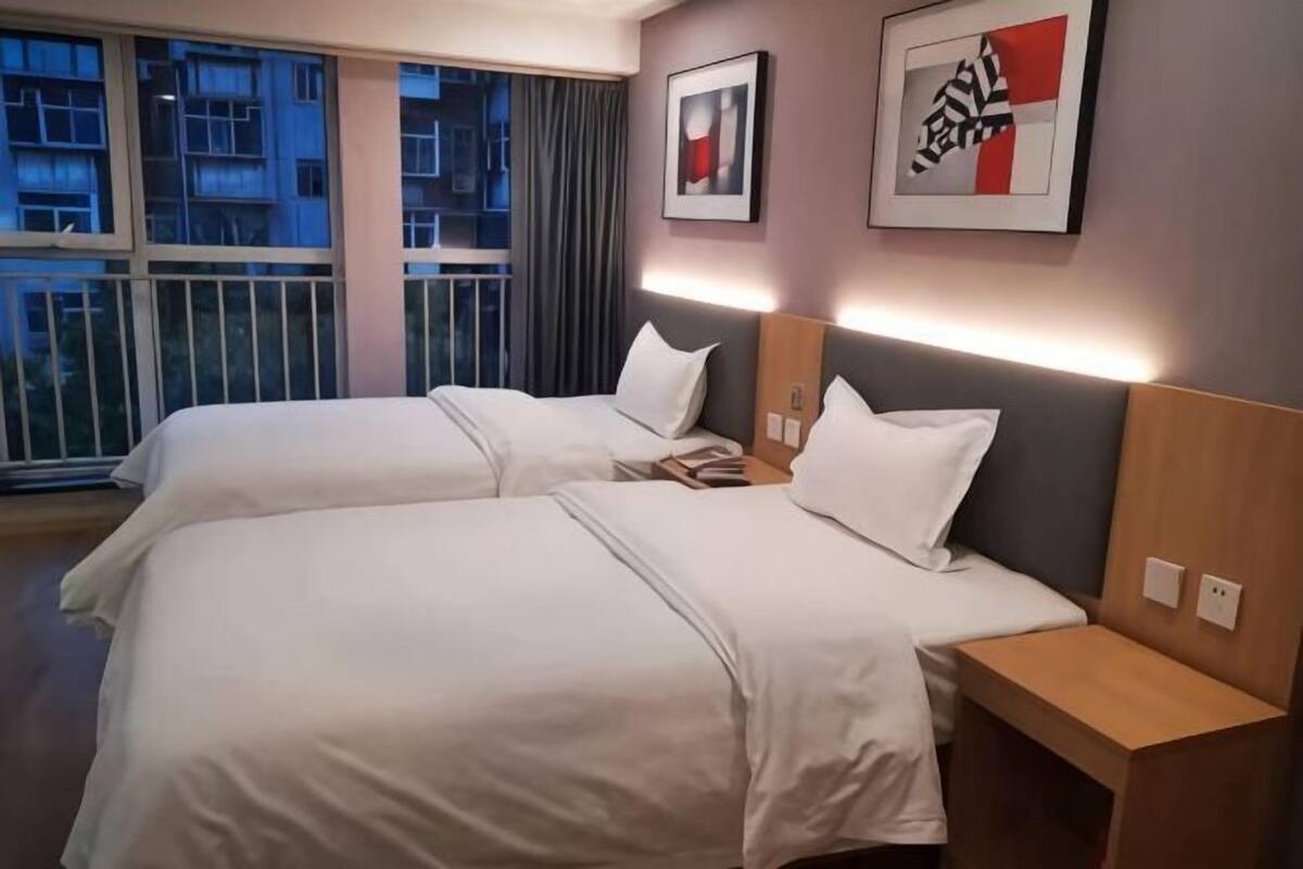 Une chambre d’hôtel avec deux lits, une table de chevet et une fenêtre donnant sur des immeubles.