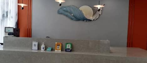 A reception desk with a grey countertop, a wall-mounted sculpture, and a red accent wall.
