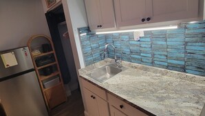 Una cocina con gabinetes de madera, un refrigerador de acero inoxidable, un lavamanos con un grifo moderno y salpicadero con azulejos azules.