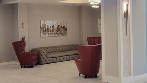Un interior moderno con un sofá modular, dos sillas rojas, un armario blanco e iluminación empotrada en el techo.