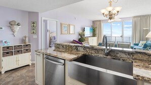 A kitchen with a granite countertop, stainless steel sink, and a dining area with a view.