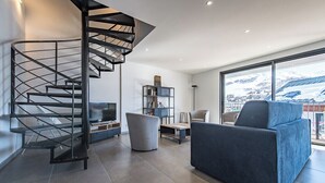 Een moderne woonkamer met een spiltrap, een groot raam met uitzicht op sneeuw, een blauwe bank en een boekenkast.
