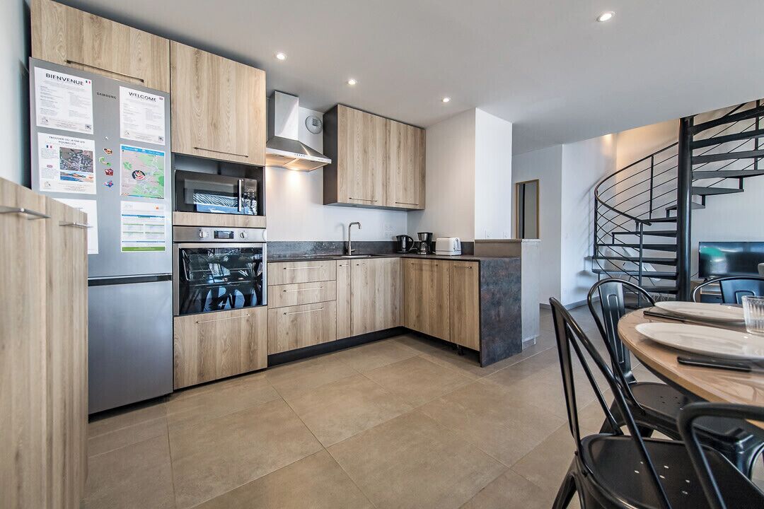 Cocina moderna con armarios de madera, electrodomésticos de acero inoxidable y un comedor con una silla y una mesa negros.