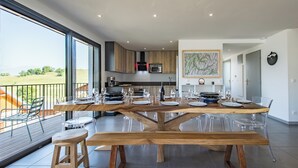 Eine moderne Küche mit großem Esstisch, gedeckter für sechs Personen, klaren Gläserstühlen und Blick ins Freie.