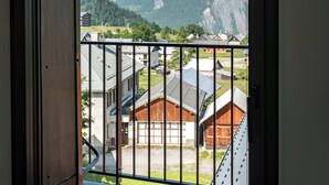 Ein Balkon mit Metallgeländer, der auf eine gebirgige Landschaft mit schneebedeckten Gipfeln und ein Dorf weiter unten blickt.