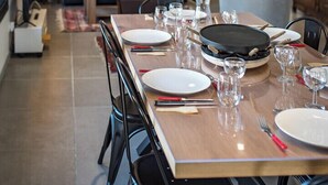 A dining area with a long table set for four, a stone wall in the background, and a sofa in the adjacent living room.