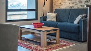 A living room with a large window, a blue sofa, a wooden coffee table, and a patterned rug.