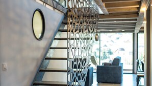 A modern staircase with a geometric metal railing, leading to a living area with a sofa and a view of the outdoors.