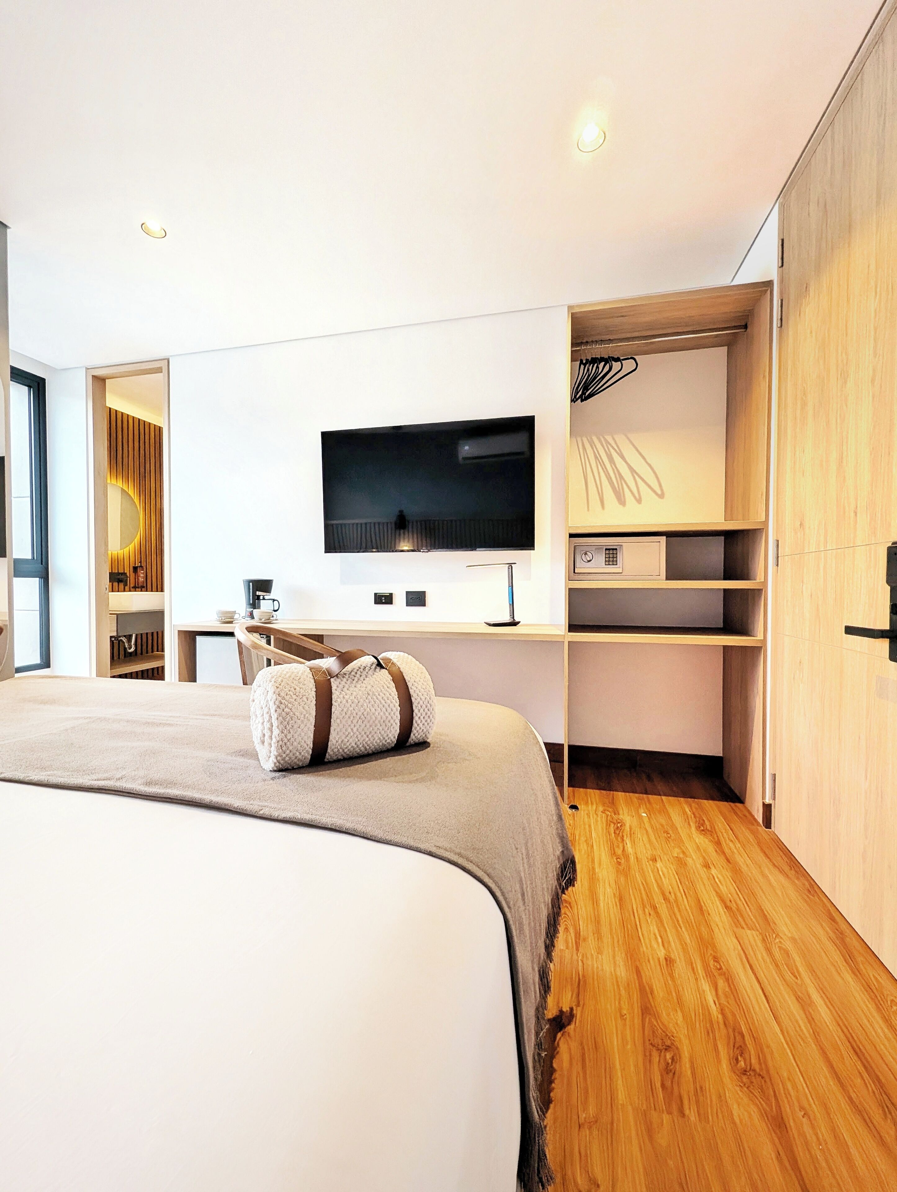 A modern bedroom with a large bed, a flat-screen TV mounted on the wall, and built-in wooden shelving.