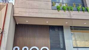 A building facade with a large 'nnoa' sign, a window with plants, and a metal utility box on the ground. - Moa Select (Medellín)