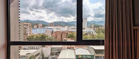 Vista a través de una ventana mostrando un paisaje urbano con edificios, una cordillera y cielo despejado.
