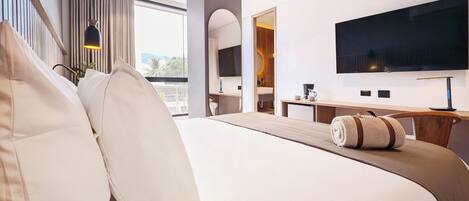 A modern hotel room with a large bed, a flat-screen TV, a desk with a chair, and a view of the outdoors.