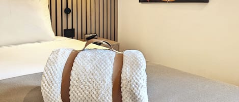 A modern hotel room with a bed, a wall-mounted lamp, and a painting of stylized leaves.