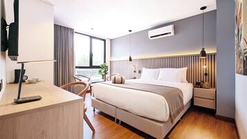 A modern hotel room with a bed, bedside table, lamp, air conditioning unit, and a view of the outdoors.