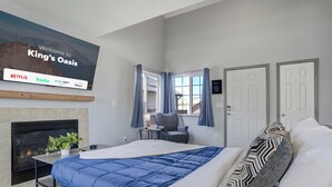A modern hotel room with a large bed, a fireplace, a TV displaying streaming services, and a view of the outdoors. - Peaceful Family Retreat w/ Pool Near Colorado Springs & Airport (Colorado Springs)