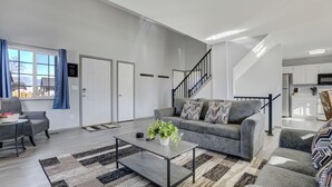 A modern living room with a grey sofa, a coffee table, and a staircase leading to the kitchen. - Peaceful Family Retreat w/ Pool Near Colorado Springs & Airport (Colorado Springs)