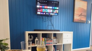 Een kamer met een blauwe muur, een flatscreen televisie aan de wand, een glazen tafel met een onderzetter en een glas bier, een boekenkast en een ingelijste foto.