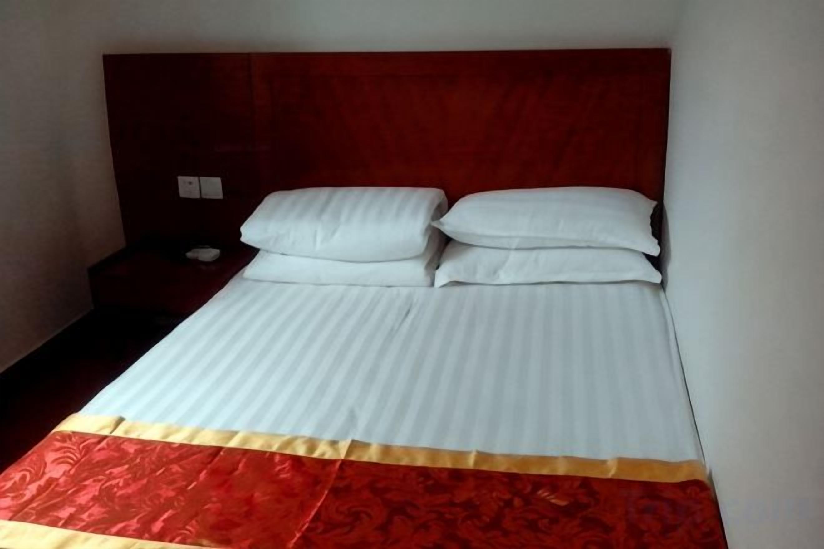 A single bed with white bedding and a red and gold accent at the foot of the bed.