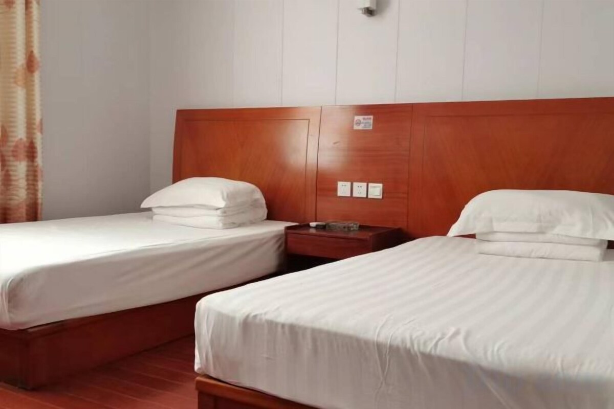 Habitació d'hotel amb dos llits individuals, amb capçaleres de fusta i una petita taula de nit amb una làmpada.