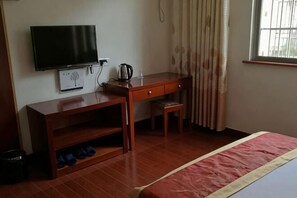 Habitación de hotel con cama, escritorio de madera, televisor y ventana con cortinas.