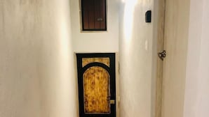 A narrow hallway with a tiled floor, a wooden door with a metal handle, and a small window above the door. - Suites Santa Noche (San Miguel de Allende)