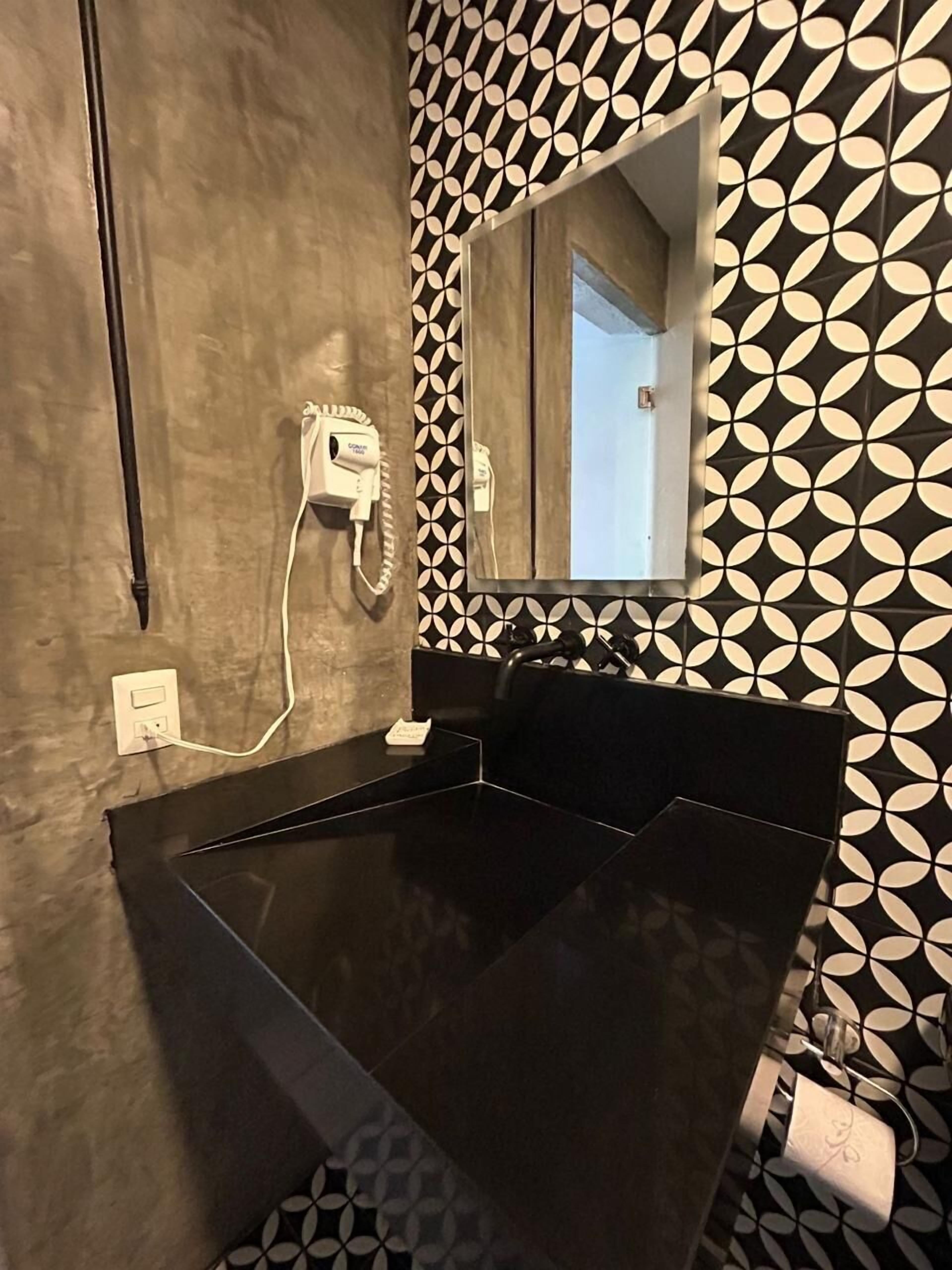 A bathroom with a black sink, a hairdryer, and a mirror.