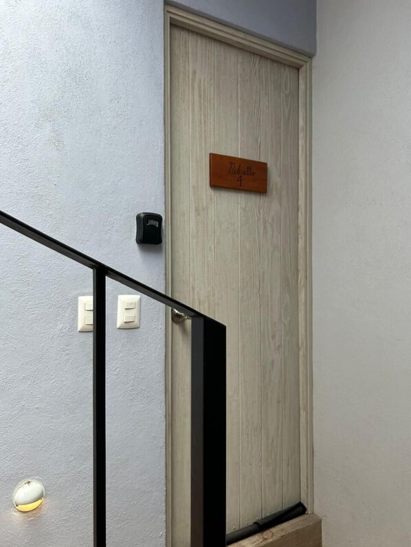 Una puerta de madera con una placa, un dispositivo de seguridad negro y una lámpara moderna.