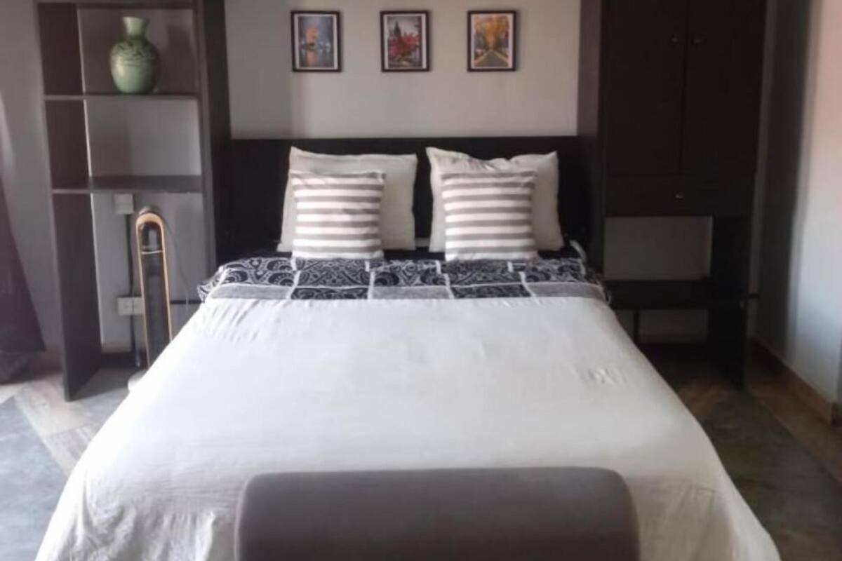 Ein Schlafzimmer mit einem großen Bett, einem Nachttisch, einer Lampe, einem Regal mit einer Vase und drei gerahmten Bildern an der Wand.