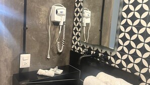 A bathroom with a black sink, a mirror, and two hair dryers mounted on the wall. - Suites Santa Noche (San Miguel de Allende)