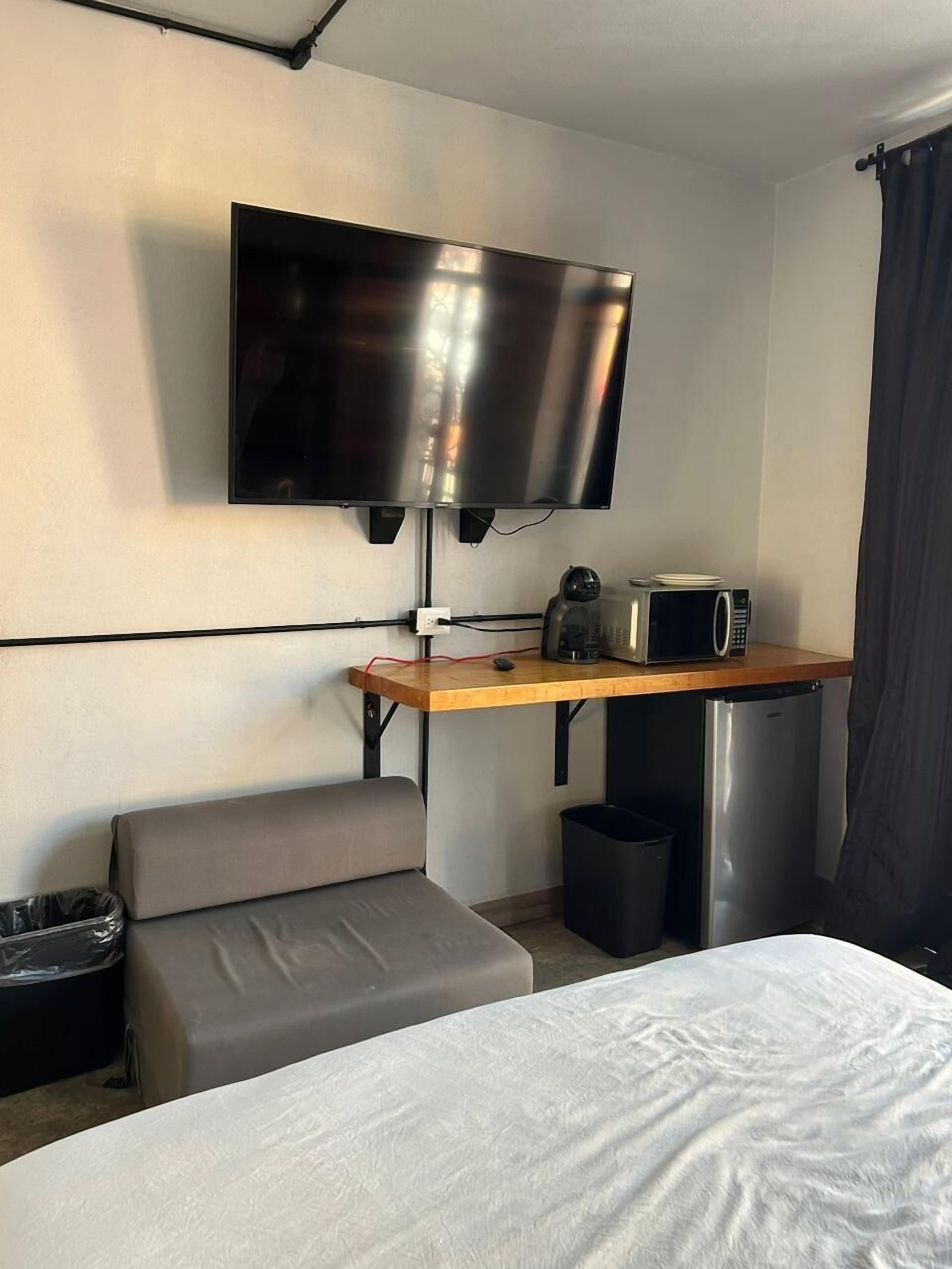A compact hotel room with a bed, a small seating area, a desk with a television, a coffee maker, and a microwave.