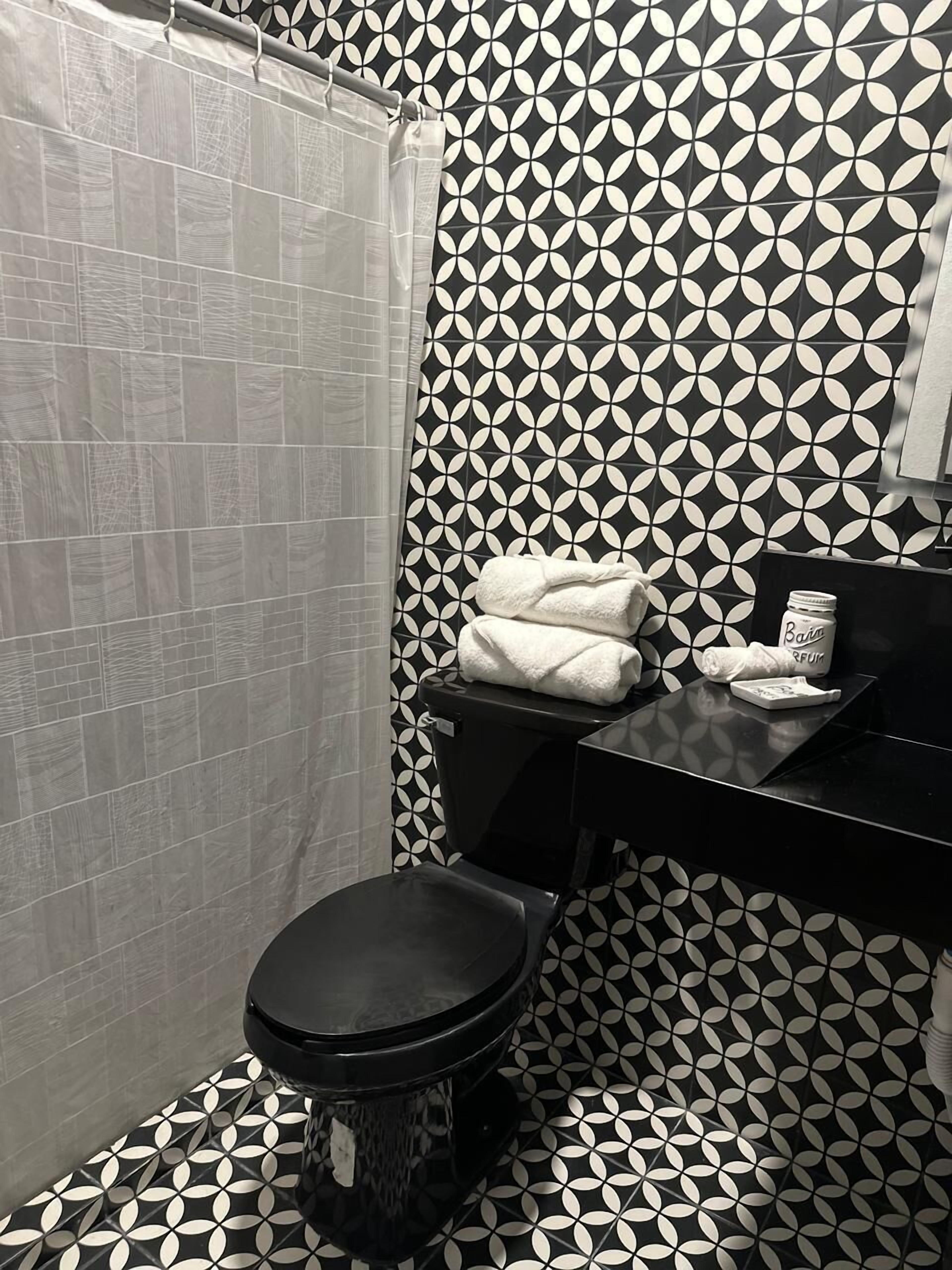 A bathroom with a black and white patterned tile wall, a black toilet, and a white towel on the sink.