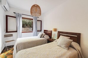 A bedroom with two beds, a wooden bench, a small table, and a hanging light fixture.