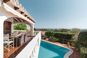 A poolside area with a view of the sea, outdoor furniture, and a pergola structure.