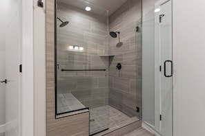 Un espace de douche entièrement vitré, doté d’une porte en verre, d’un banc en verre et d’un pommeau de douche.
