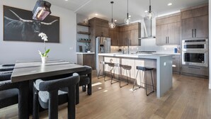 A modern kitchen with wooden cabinets, stainless steel appliances, a central island with bar stools, and pendant lighting. - East Klaim Drive Departments (Hideout)