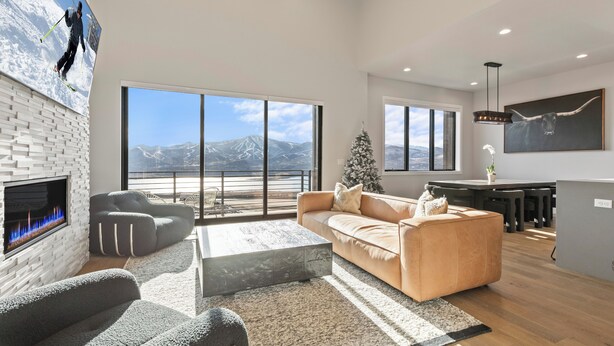 A spacious living room with a fireplace, large windows, a cozy sofa, and a dining area. - East Klaim Drive Departments (Hideout)