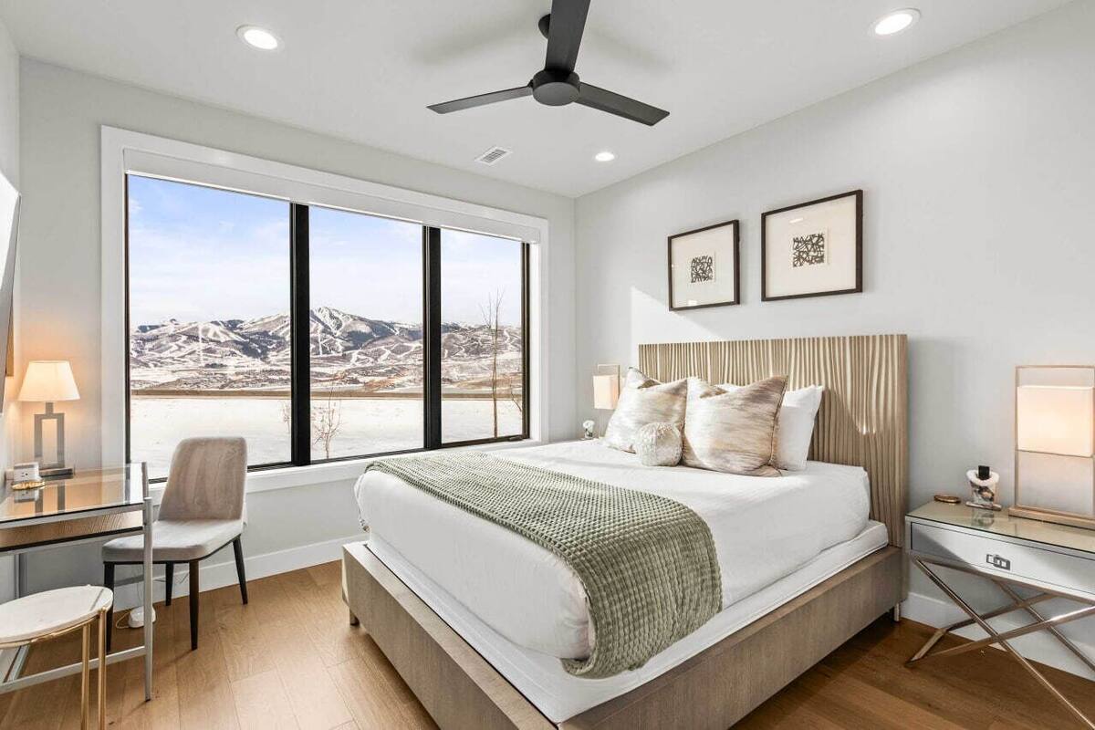 Een moderne slaapkamer met een groot bed, een bureau en een stoel. Er hangen twee ingelijste foto's aan de muur, en er is een plafondventilator.