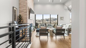 A spacious living room with a large window, a staircase, and a view of mountains. - East Klaim Drive Departments (Hideout)