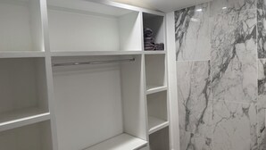 A walk-in closet with white shelving and marble-patterned walls.